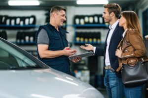 Happy auto repairman communicating with young couple in a workshop